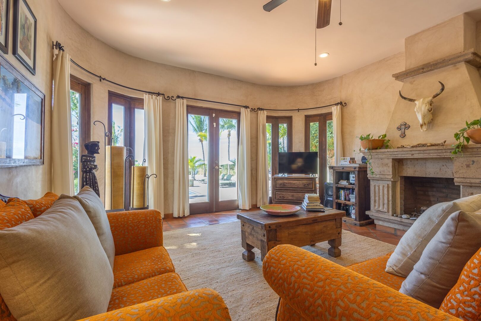 Living room with orange sofas, stone fireplace, and pool views